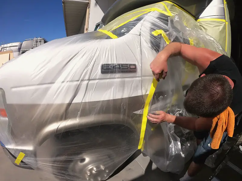 Technician taping plastic over an RV to mask it for paint